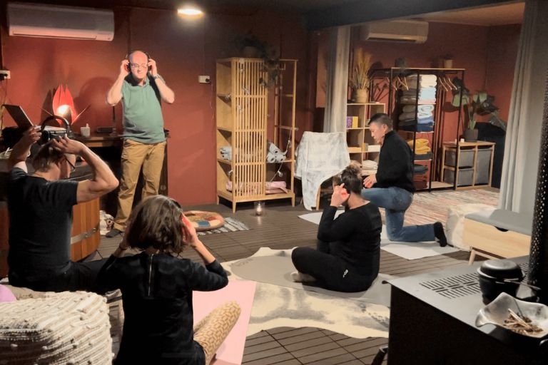 Participants engaging in a guided breathwork session in the wellness space at Eltham Wellness Centre. The room features soft lighting, a wooden hot tub, meditation props, and an instructor leading the practice.