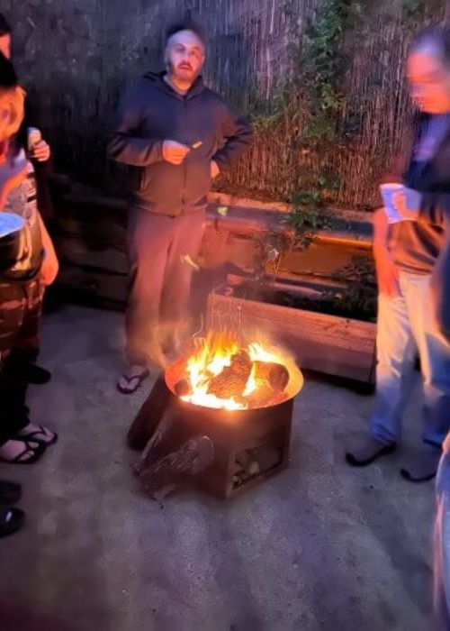 A group of people enjoying an evening around a cozy outdoor firepit at Eltham Wellness Centre. The warm glow of the fire contrasts with the cool night air, creating a communal and relaxing atmosphere.