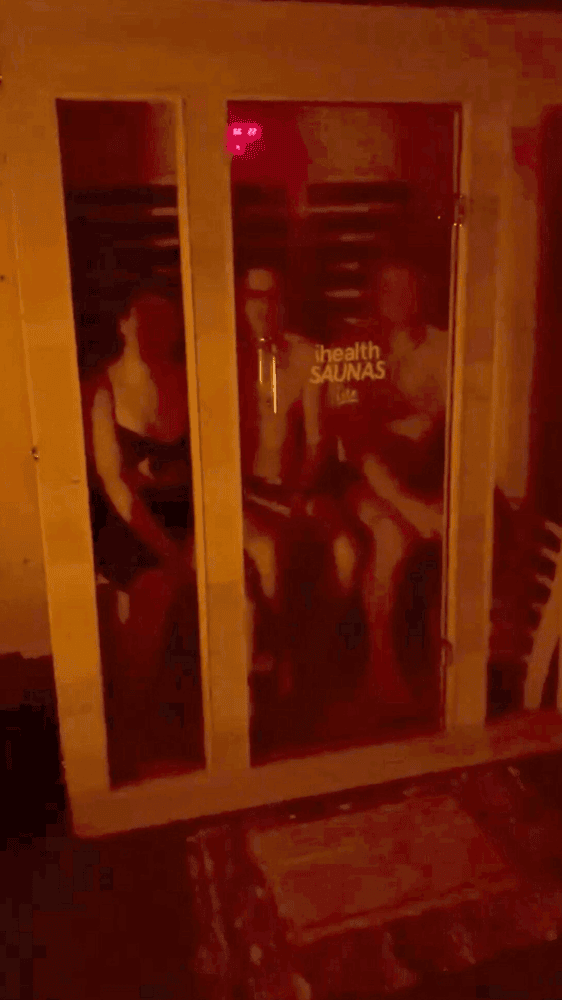 Three people sitting inside a warmly lit infrared sauna at Eltham Wellness Centre, immersed in the deep heat therapy. The red glow from the infrared panels enhances relaxation and promotes detoxification. The cozy ambiance and wooden sauna cabin create an ideal setting for recovery and wellness.