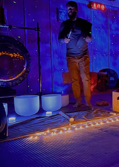 A sound healing practitioner leading a session at Eltham Wellness Centre, surrounded by singing bowls, a gong, and soft ambient lighting. The dimly lit room with fairy lights enhances the meditative and calming experience.