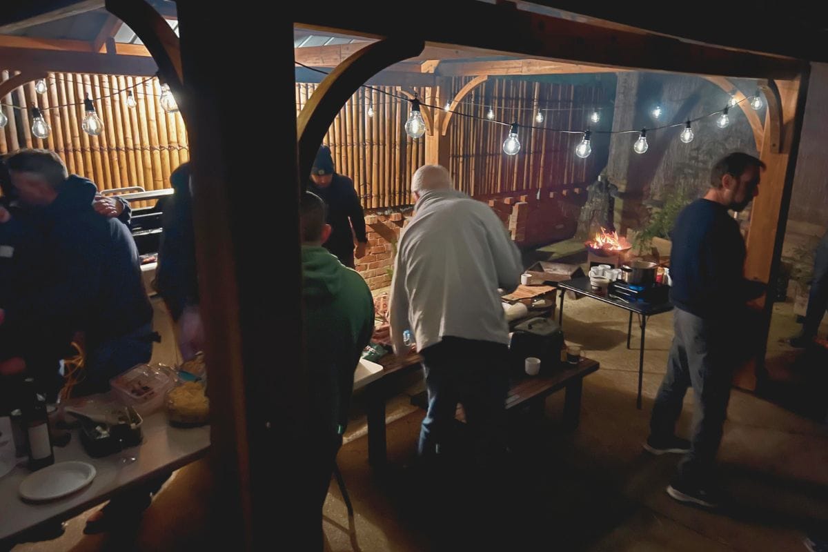 Evening event in the outdoor area at Eltham Wellness Centre, featuring guests gathered under festoon lights around food tables and a fire pit in a covered courtyard.