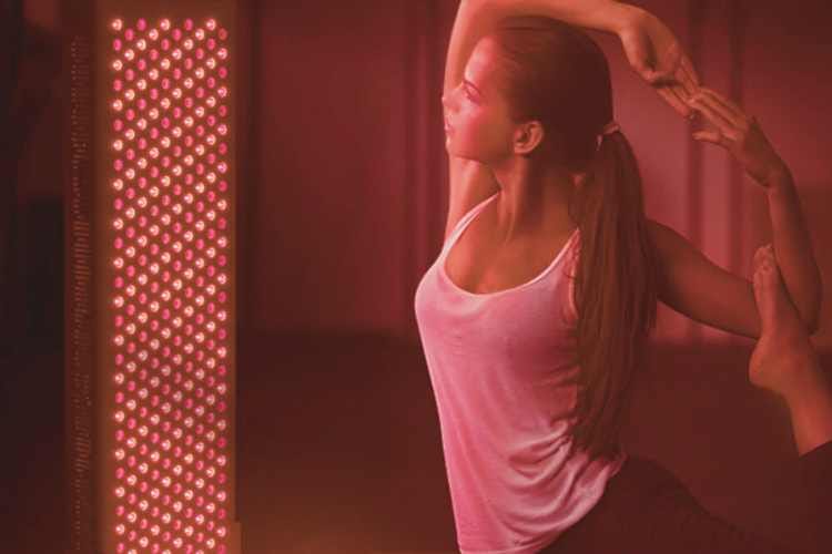 Red Light Therapy for Flexibility and Performance – Eltham Wellness Centre A woman in an active stretch pose in front of a red light therapy panel, highlighting the use of red light for flexibility, performance, and muscle recovery
