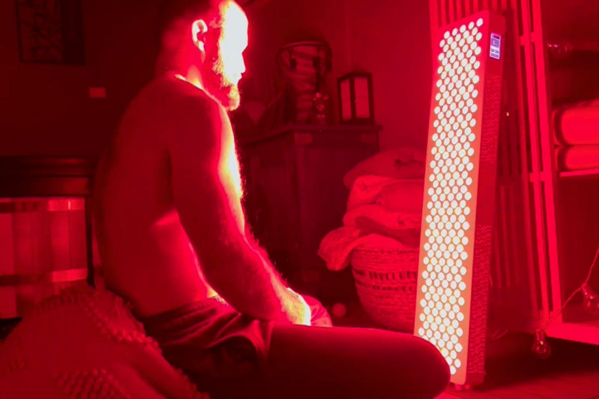 Red light therapy Eltham wellness centre Man sitting shirtless in front of a red light therapy panel at Eltham Wellness Centre, promoting recovery, skin health, and relaxation in a dimly lit room.